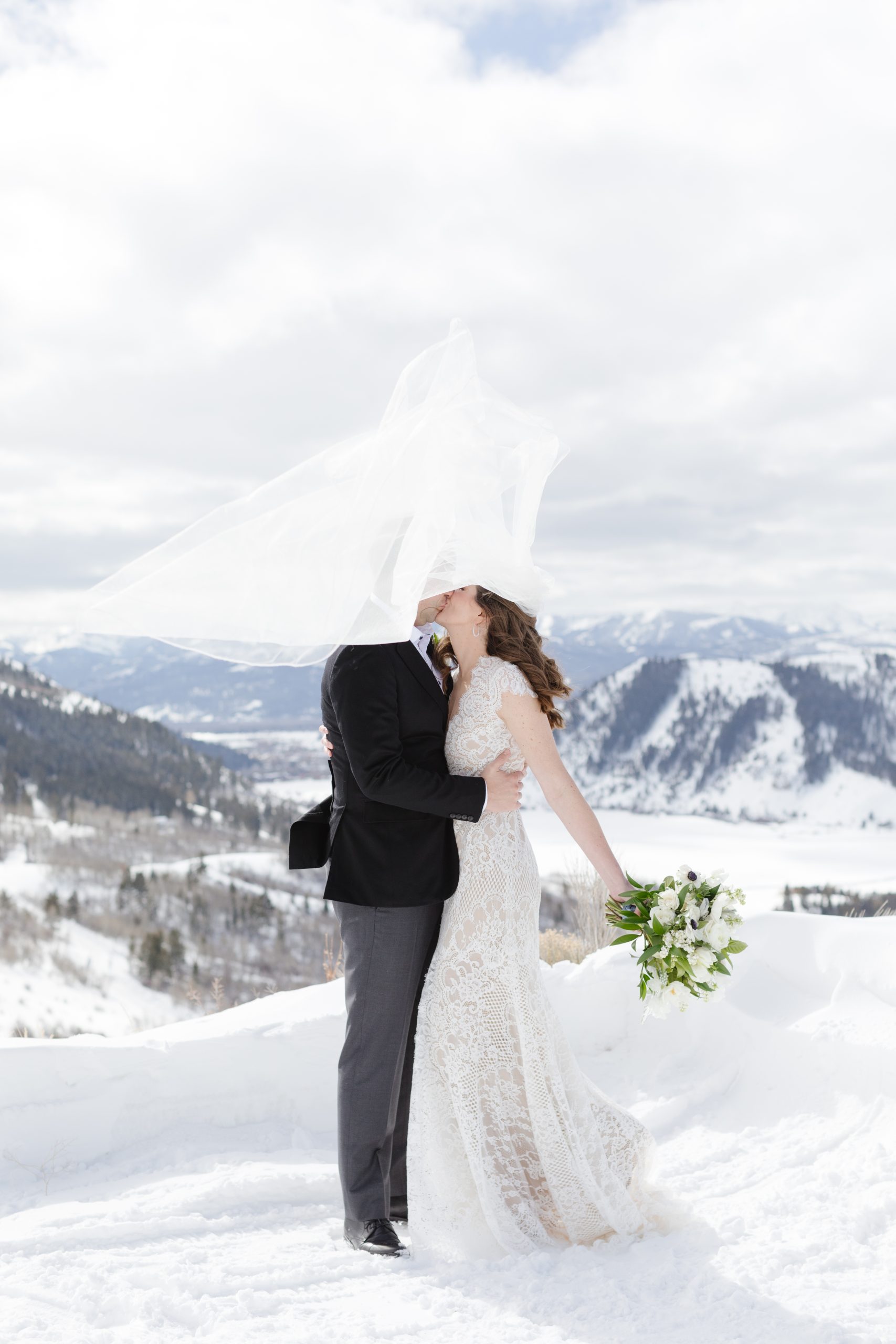 bride and groom kissing in the snow amongst the mountains