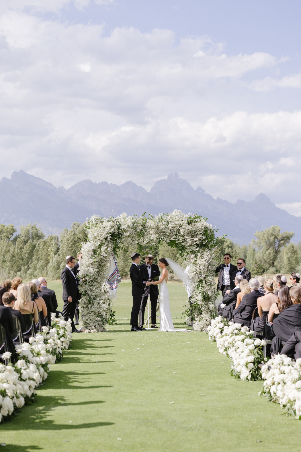 Outdoor wedding ceremony with floral arch and Teton views.