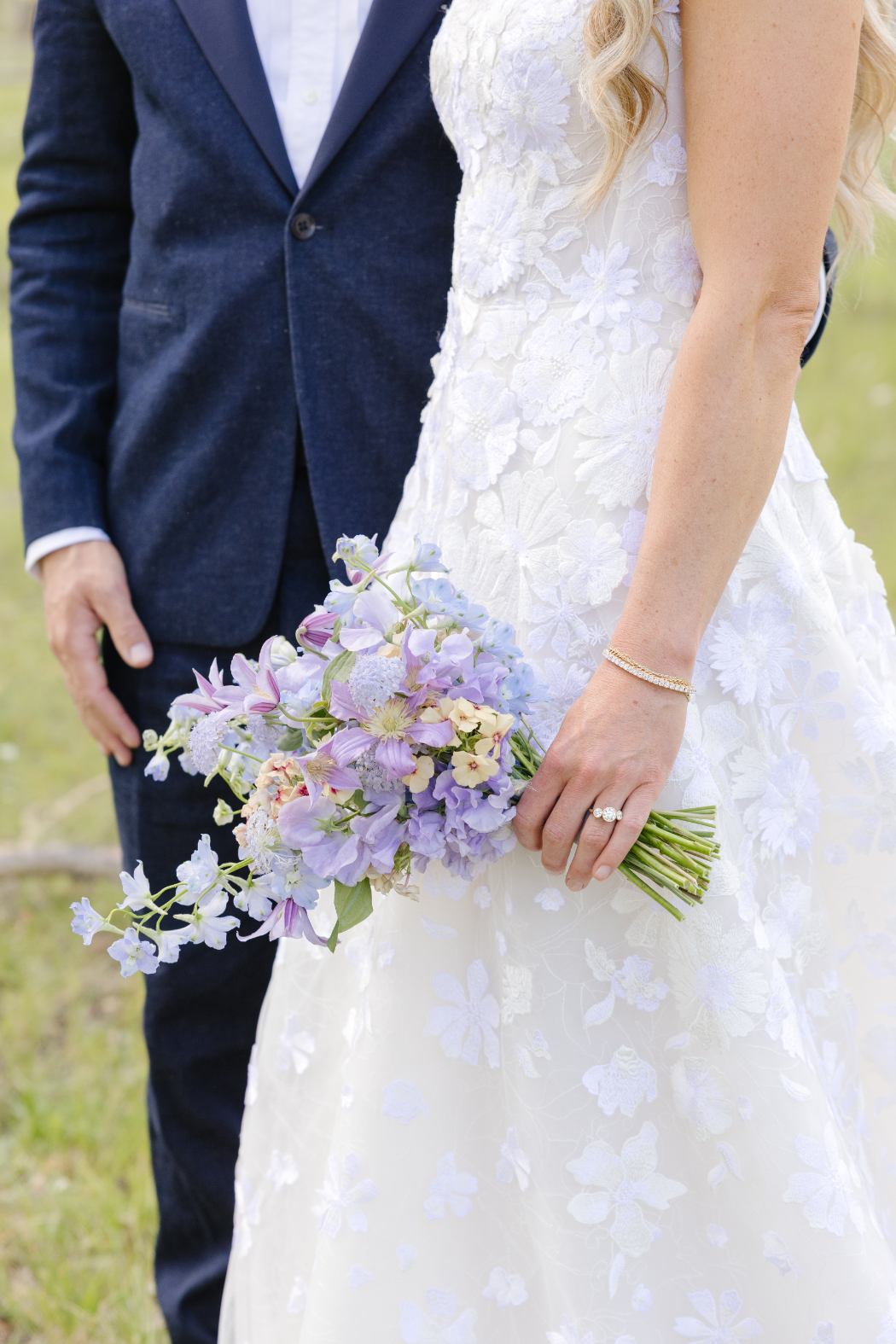 a close up shot of a bride and groom in an outdoor setting and the focus is on the brides purple and peach bouquet
