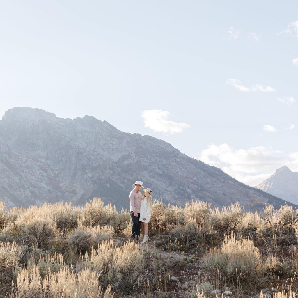 couple standing on top of a hill with alpine views in the background- engagement photo ideas