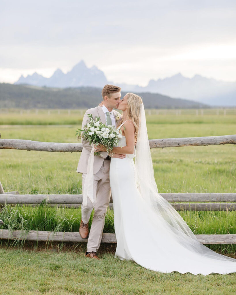 eloping-in-jackson-hole bride and groom kissing by the fence with mountains in the background while Eloping with Family