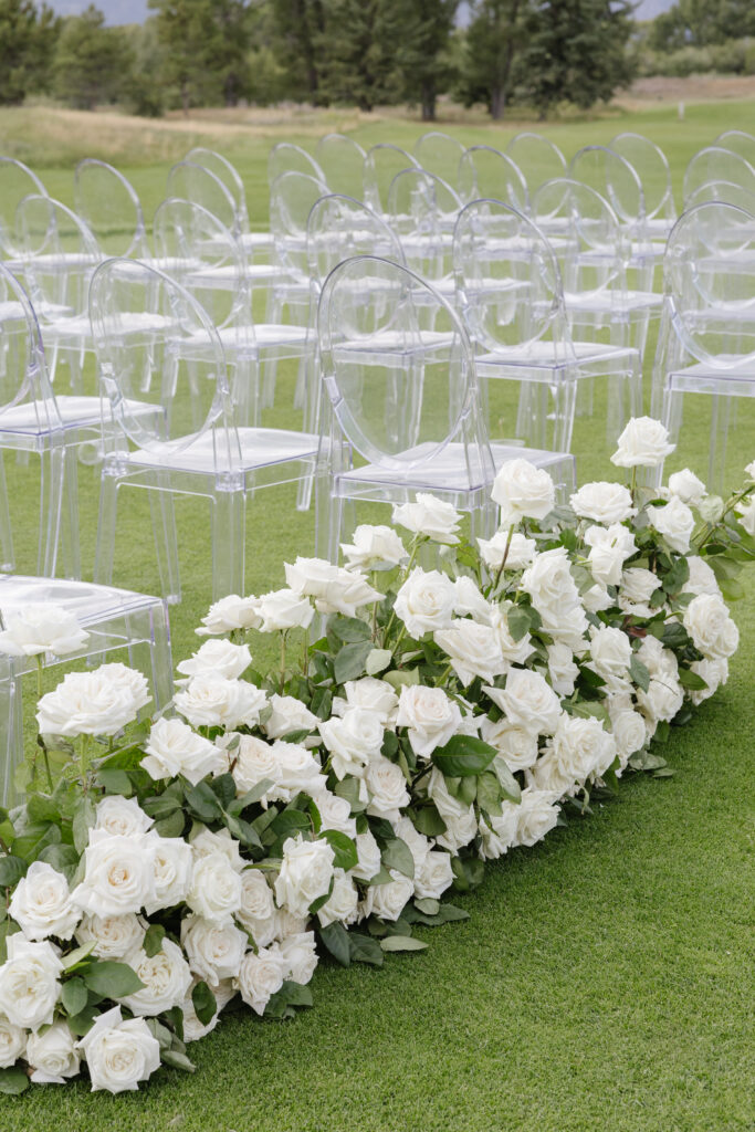 Elegant ceremony setup at Jackson Hole Golf and Tennis Club with white roses and ghost chairs.