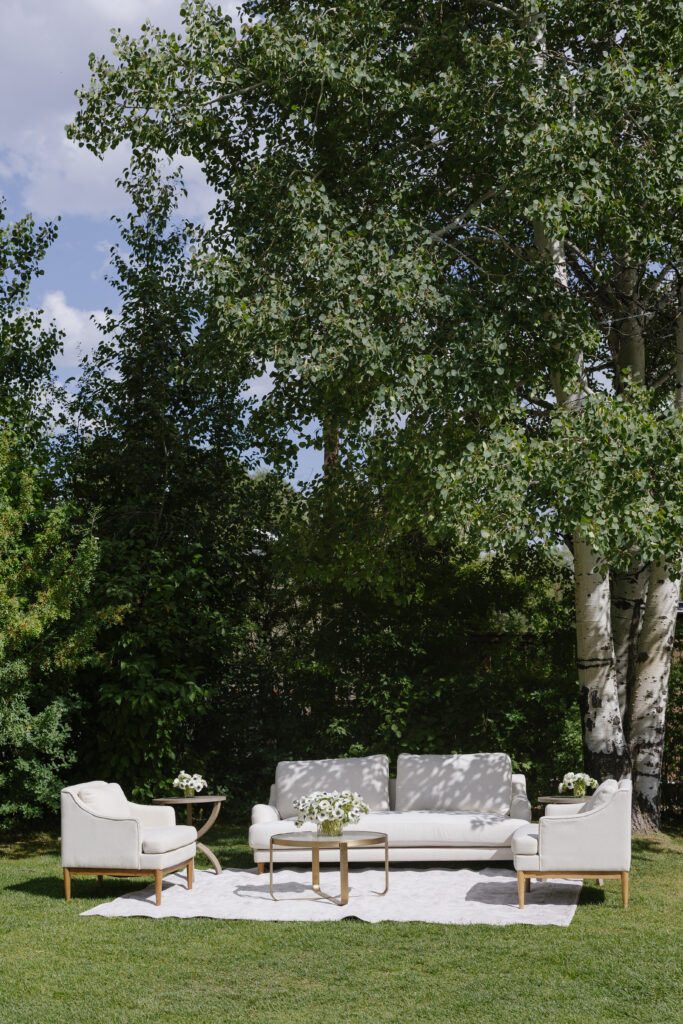 Cozy outdoor lounge setup with white furniture and floral accents, perfect for mingling beneath the trees.
