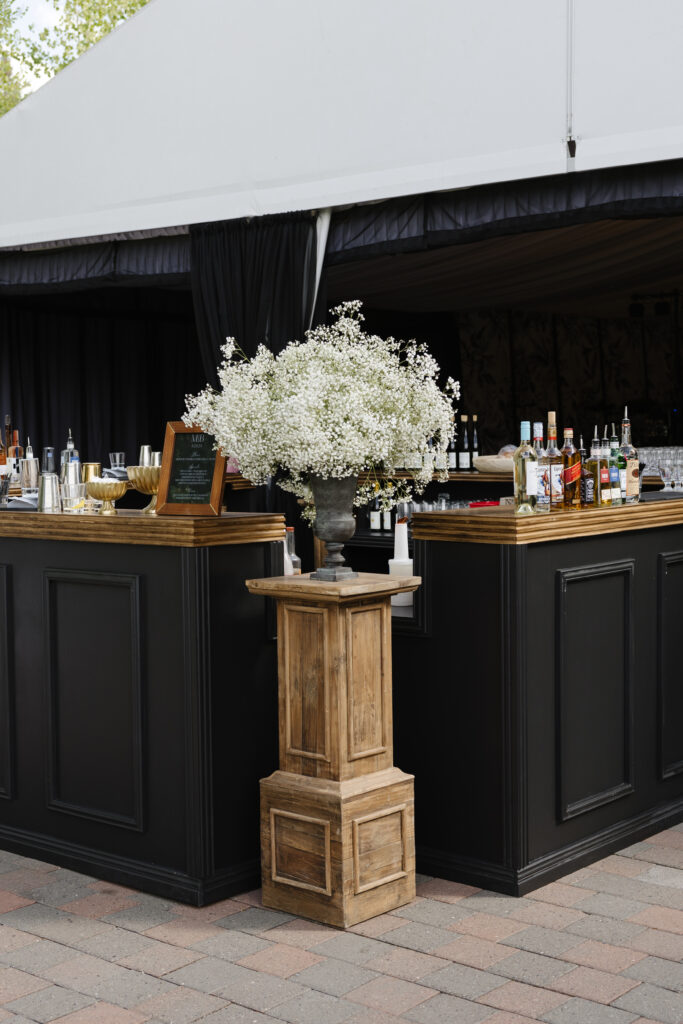 Stylish outdoor bar setup with bold black paneling, wood accents, and a lush baby's breath arrangement.