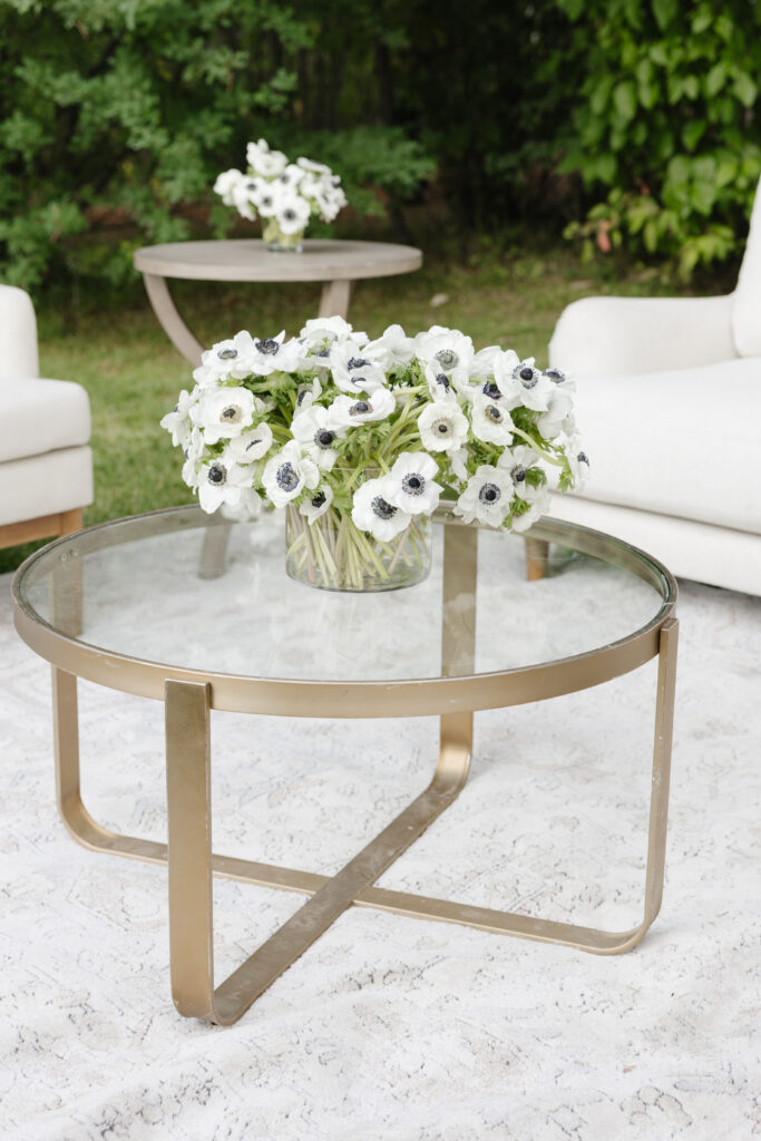 Modern glass coffee table with a white anemone arrangement, adding charm to the outdoor lounge area.