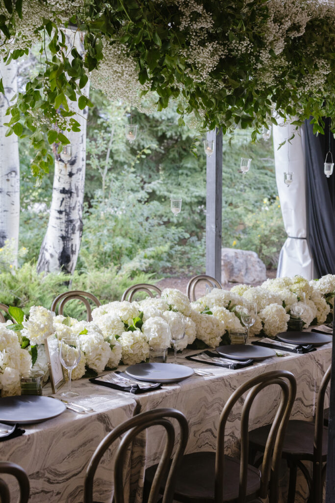Lush floral tablescape with hanging greenery and candlelight, set against a serene woodland backdrop.