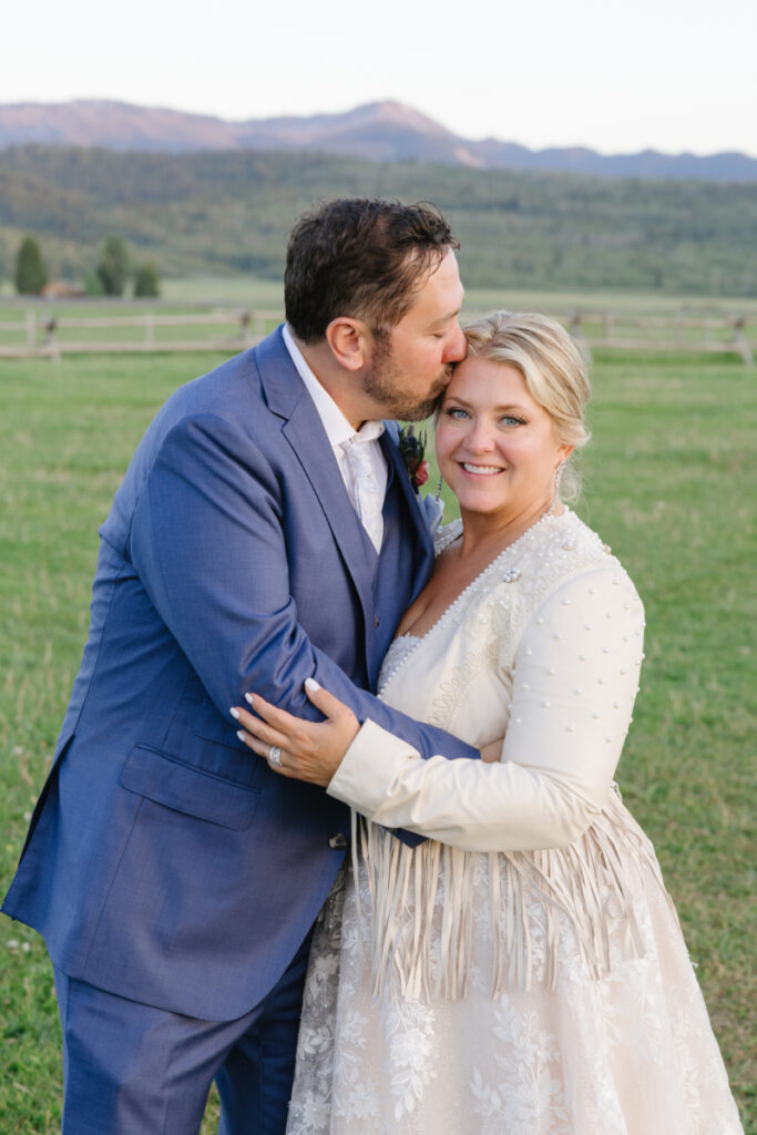 Groom kisses bride on the forehead during golden hour portraits.
