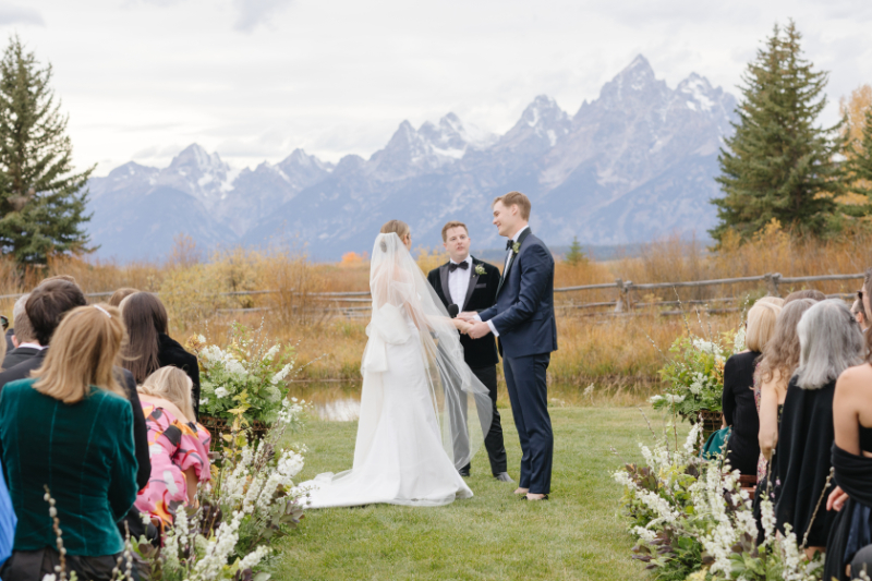 Bride and groom exchange vows with breathtaking views of the Tetons Rendezvous Peak towering behind them at their Moose Creek Ranch wedding.