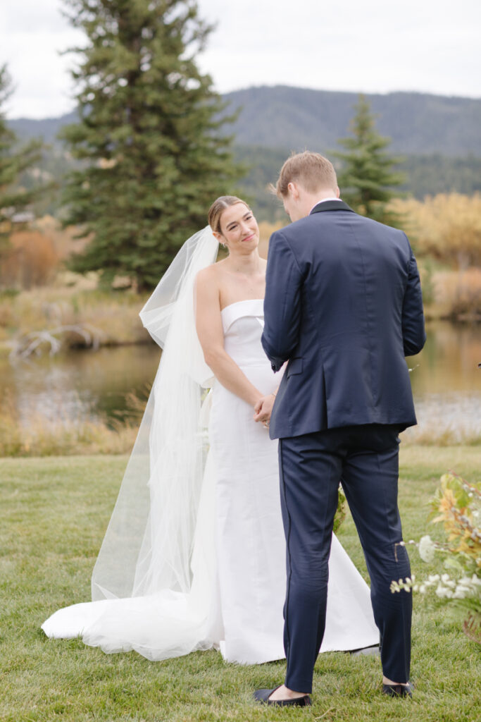 Bride looks at groom lovingly as groom reads his vows to her during wedding ceremony.