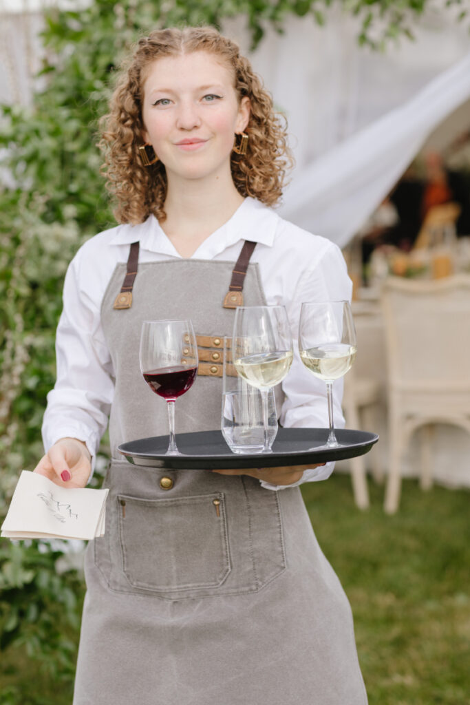 Server for a Moose Creek Ranch wedding passes red and white wine to guests during cocktail hour.