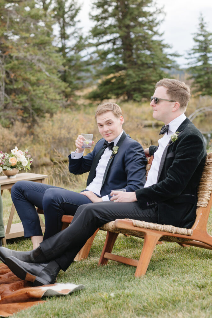 Groom sits in lounge seating as he raises his glass for a toast during cocktail hour with groomsmen.