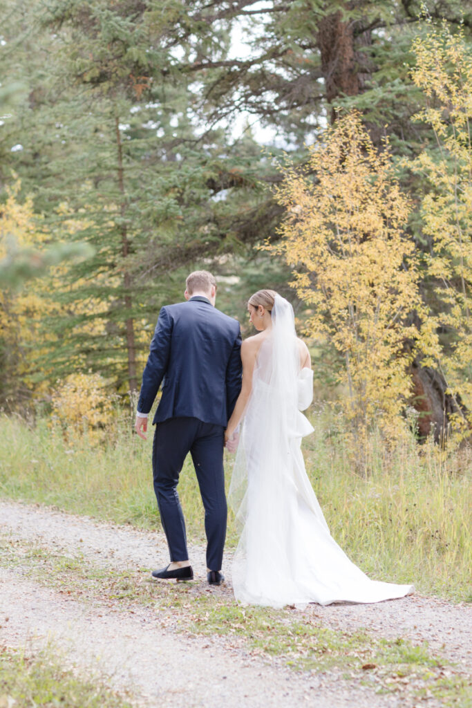 Bride and groom walk together on gravel road as their photographer captures portraits.