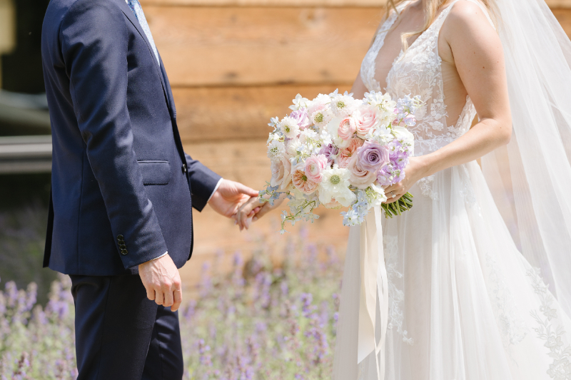 Closeup shot of bride and groom holding hands as bride holds bouquet.