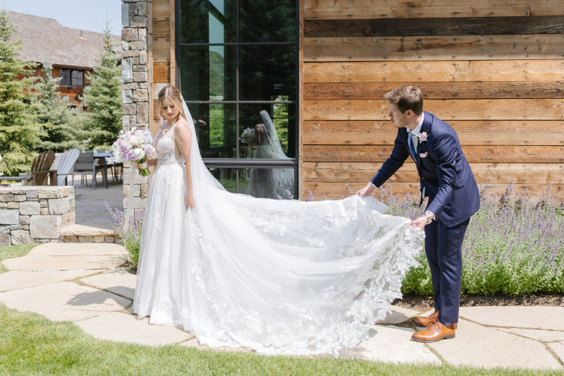 Groom fluffs brides train during portraits at their destination wedding venue in Jackson Hole.
