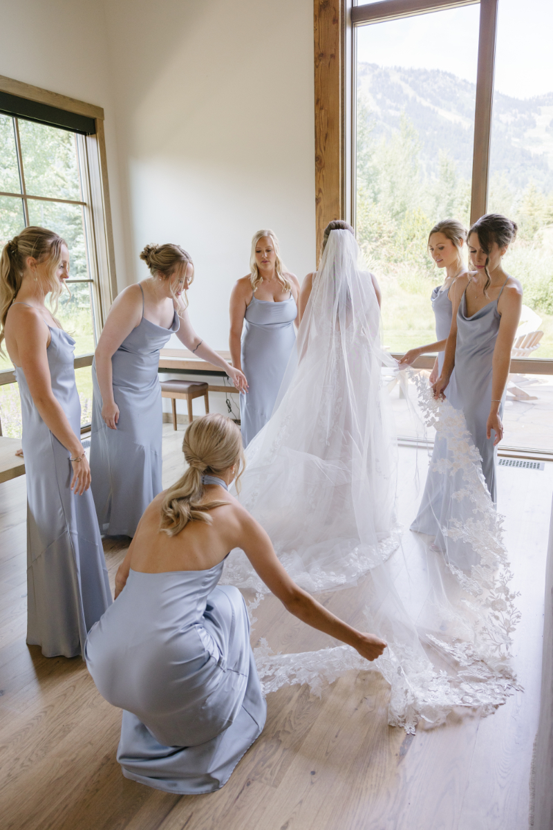 Bridesmaids surround bride during first look, while one bridesmaid fluffs bride's train.