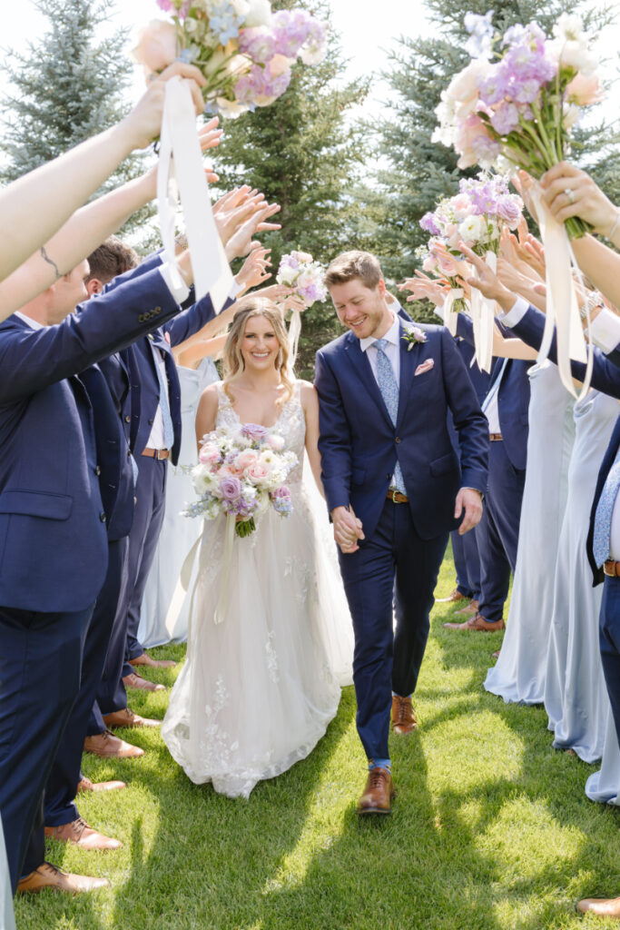 Bride and groom walk together through tunnel of their bridal party's raised hands.
