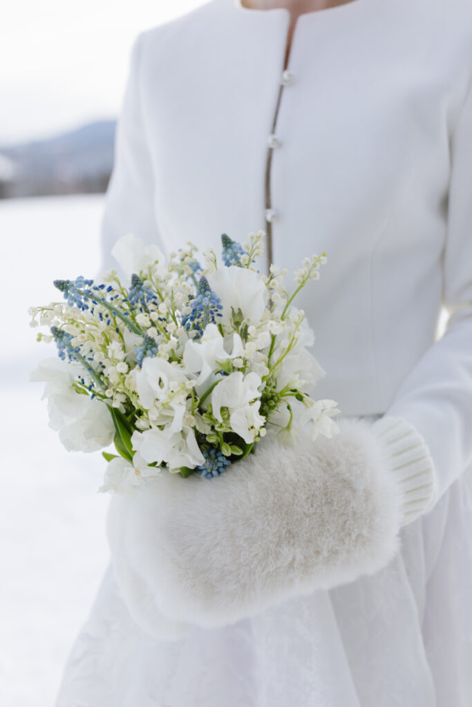 Bride holds small bouquet in her faux fur mittens. 