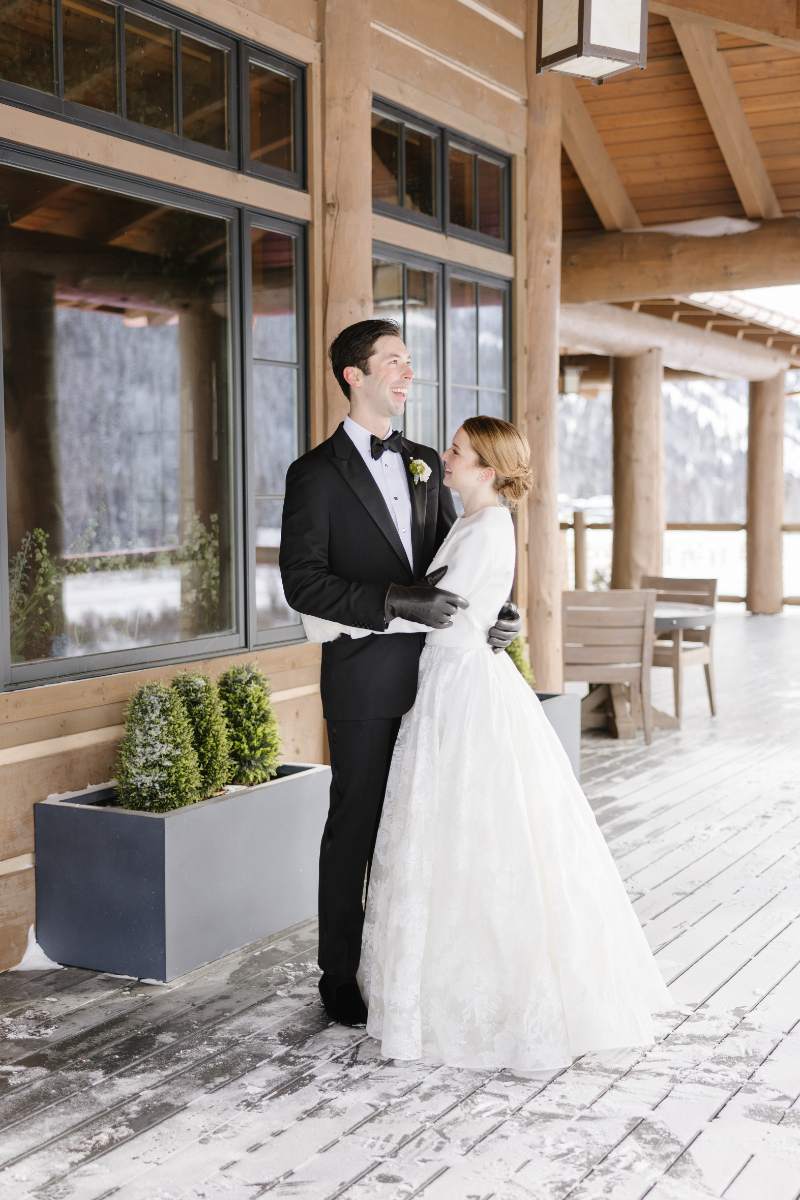 Bride and groom hug on the deck of lodge during winter elopement.