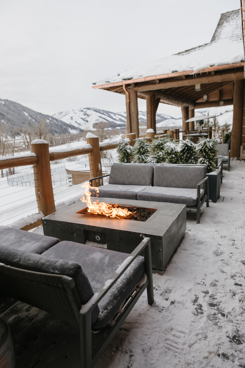 Jackson Hole lodge covered in snow, a fire going on a table surrounded by couches.