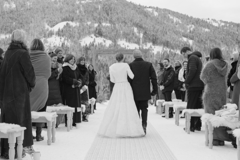 Father walks daughter down snow covered aisle in the Tetons during winter elopement.