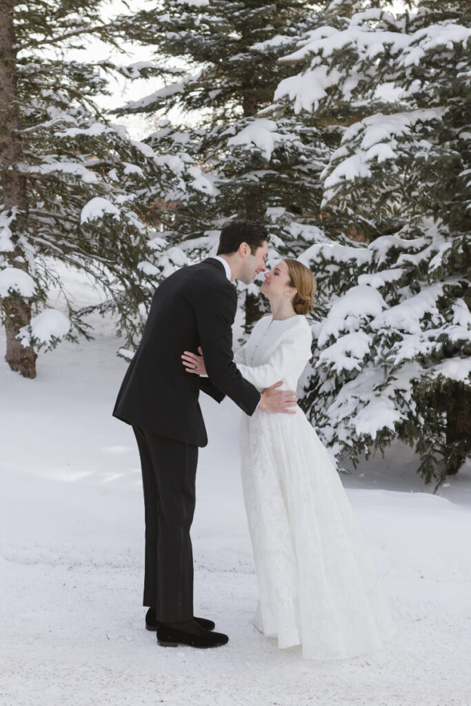 Bride and groom kiss while snow falls around them during their winter elopement in Jackson Hole.