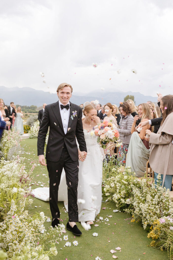 Bride and groom recess down aisle as their guest throw flower petals at them.