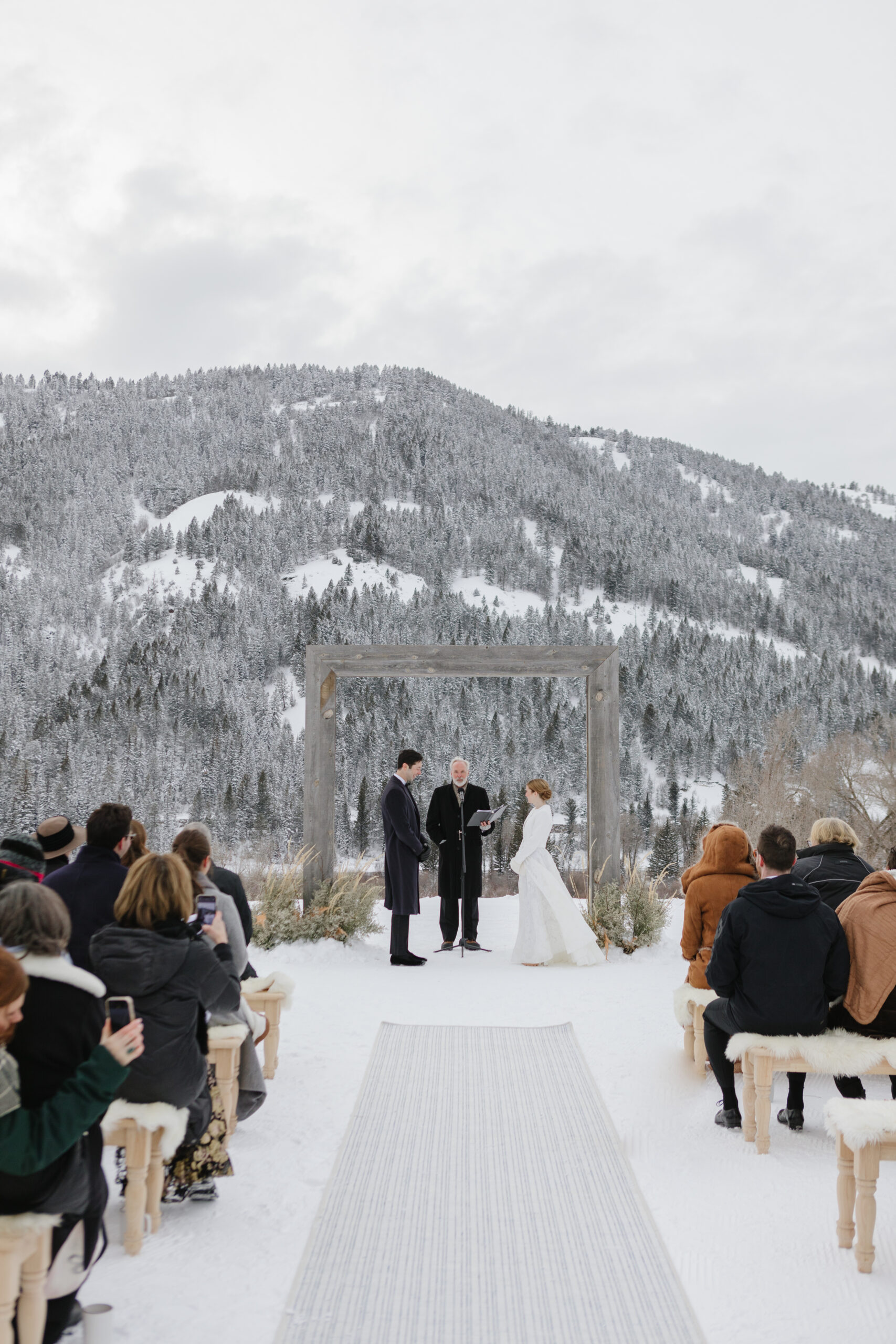 Bride and groom stand facing one another at the altar with snowy Teton mountains behind them.