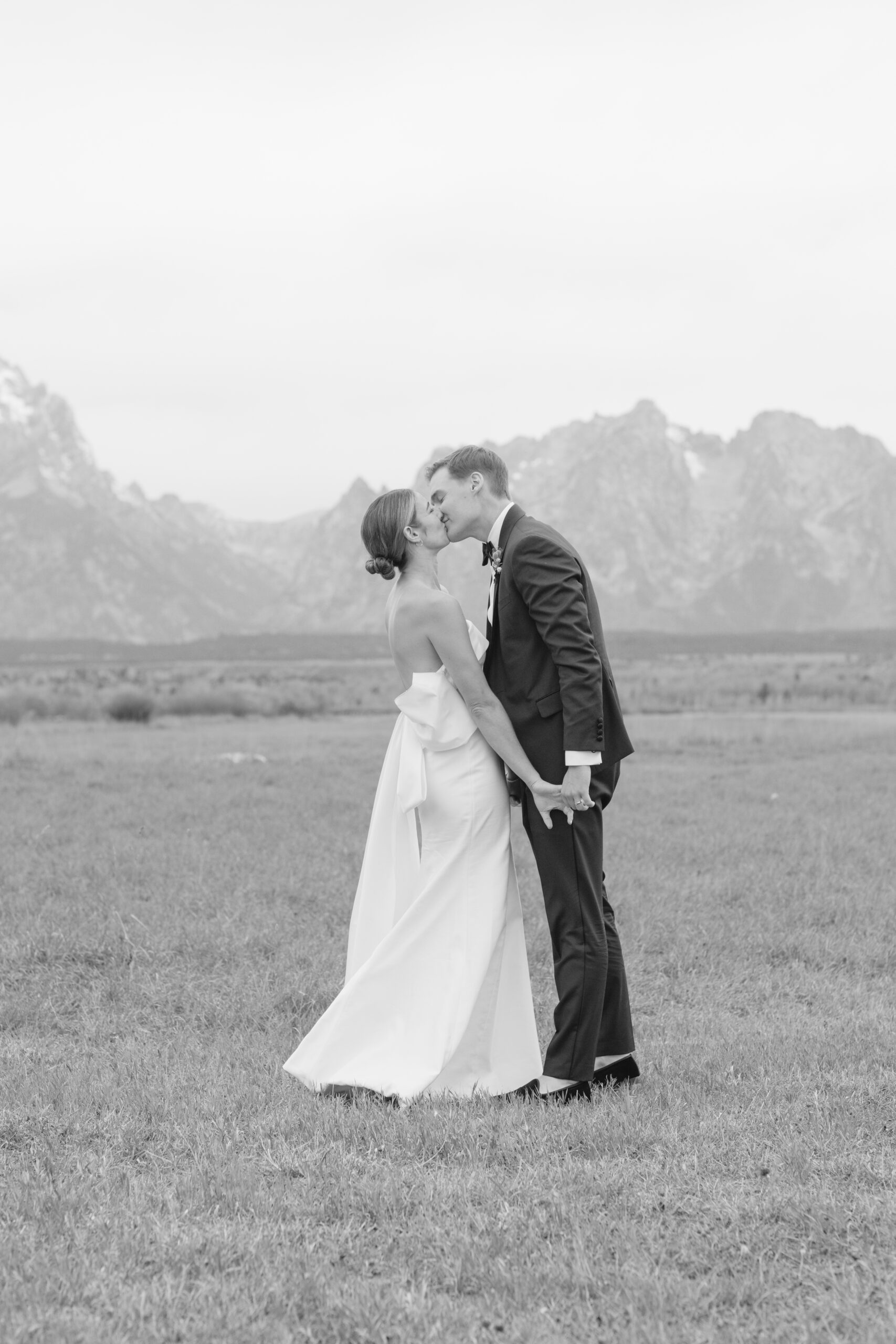 Bride and groom kiss as they stand in field in Jackson Hole.