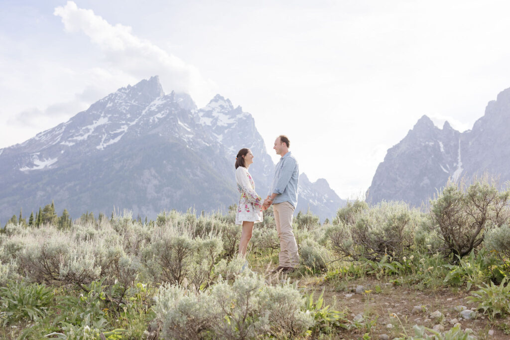 Couple stand up front of each other holding hands as they pose for their engagement photo.