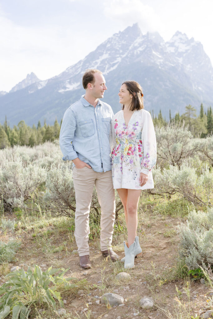 Couple stand next to each other looking at each other as they pose for their engagement photography at Jackson Hole.