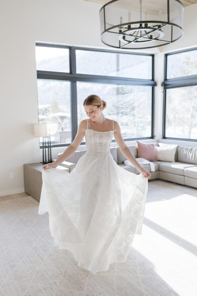 Bride inside the Snake River Sporting Club hotel room posing and showing her beautiful white gown with a smile on her face before her small venue wedding.
