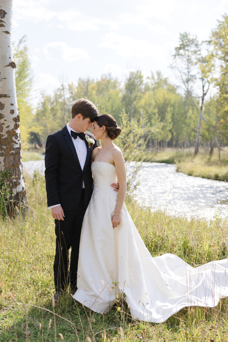 Bride and groom embracing by a river during a Grand Teton wedding with scenic mountains and greenery in the background