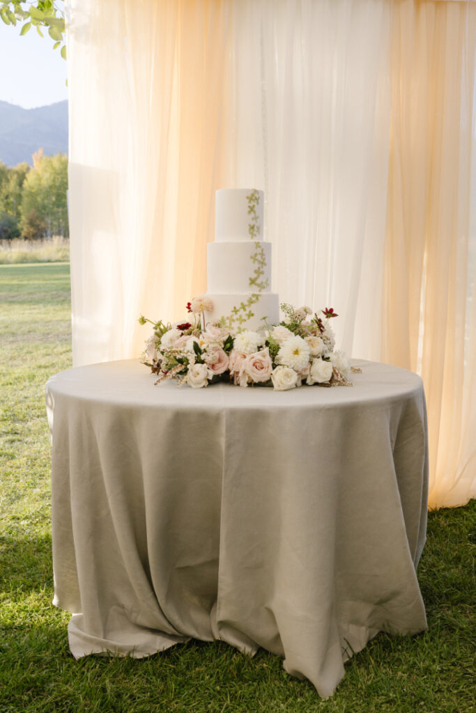 Elegant three-tier wedding cake with floral arrangement displayed at a Grand Teton wedding reception