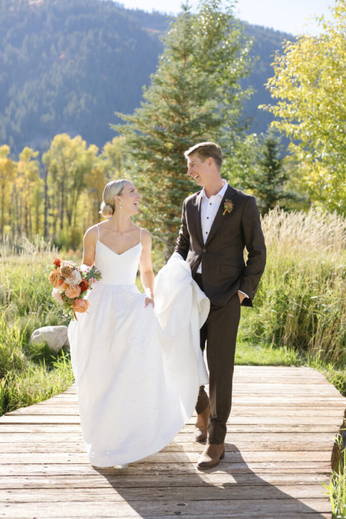 Bride and groom walking hand in hand on a wooden path during a Grand Teton wedding surrounded by greenery
