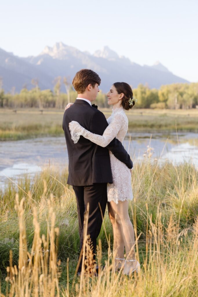 Bride and groom embracing near water with Tetons in background, photographed by Jackson Hole Photographers