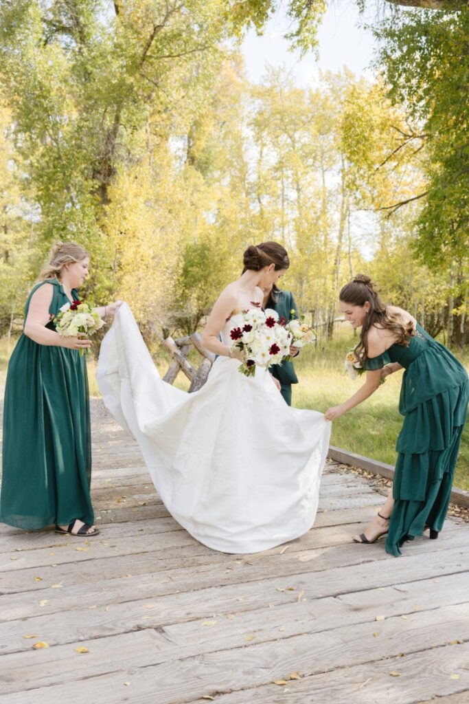 Bride with bridesmaids adjusting wedding dress outdoors in fall, captured by Jackson Hole Photographers