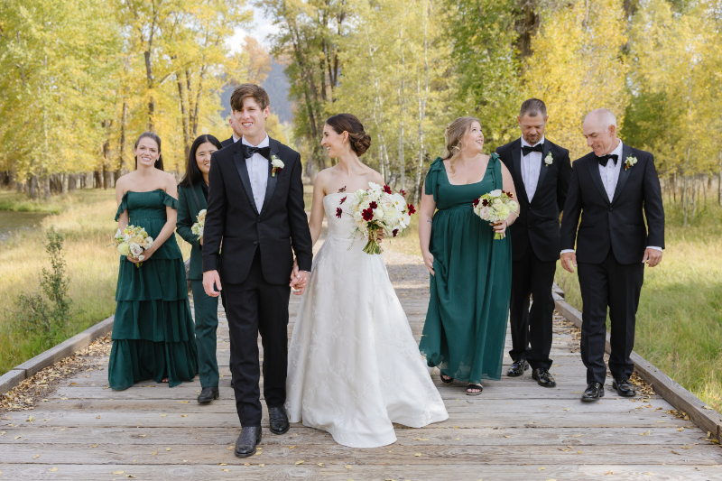Bride and Groom walking and smiling as bridesmaid and groomsman behind walking in the Snake River forest.
