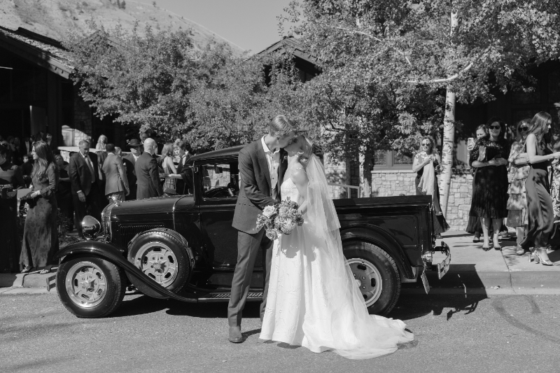 Black and White image of a Bride and Groom kissing and behind them is an old antique ford.