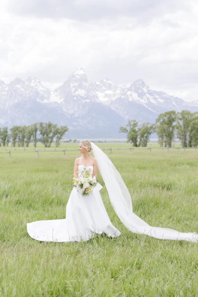 Bride looking over her shoulder and smiling as the Grand Tetons show behind her.