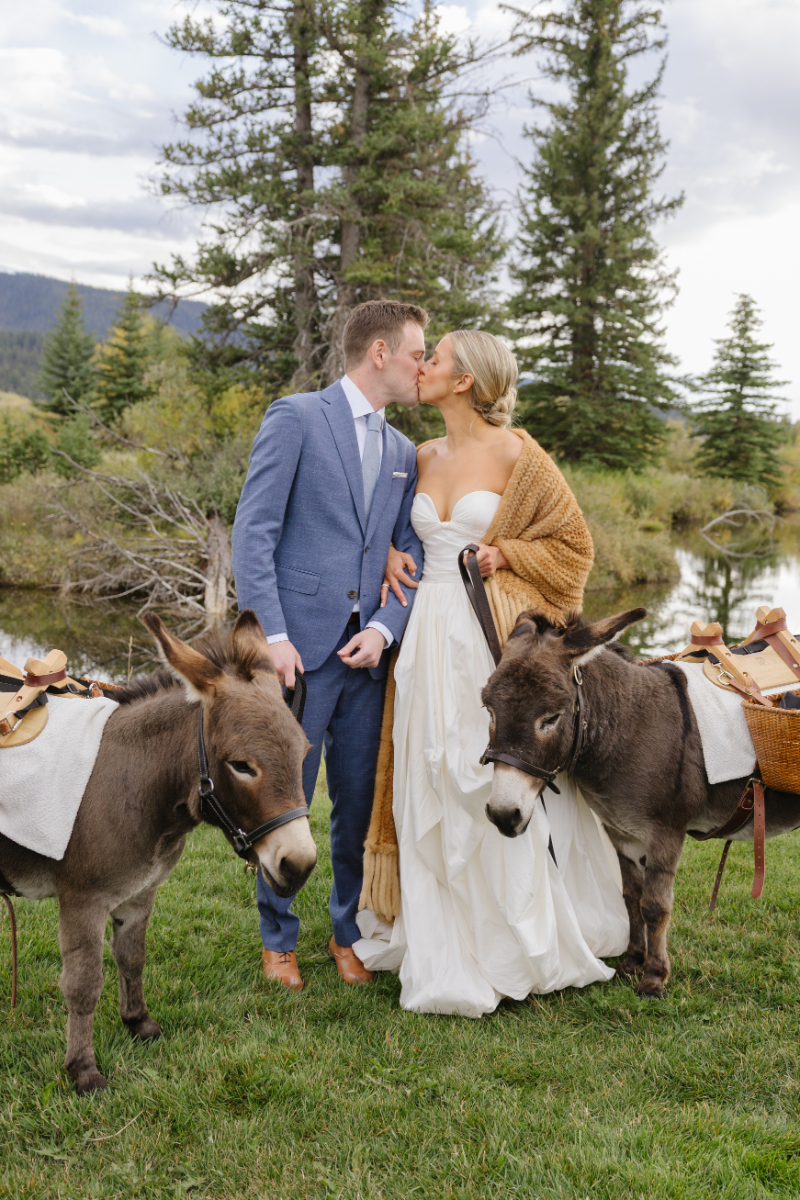 Bride and groom kissing beside donkeys at a Jackson Hole dude ranch wedding