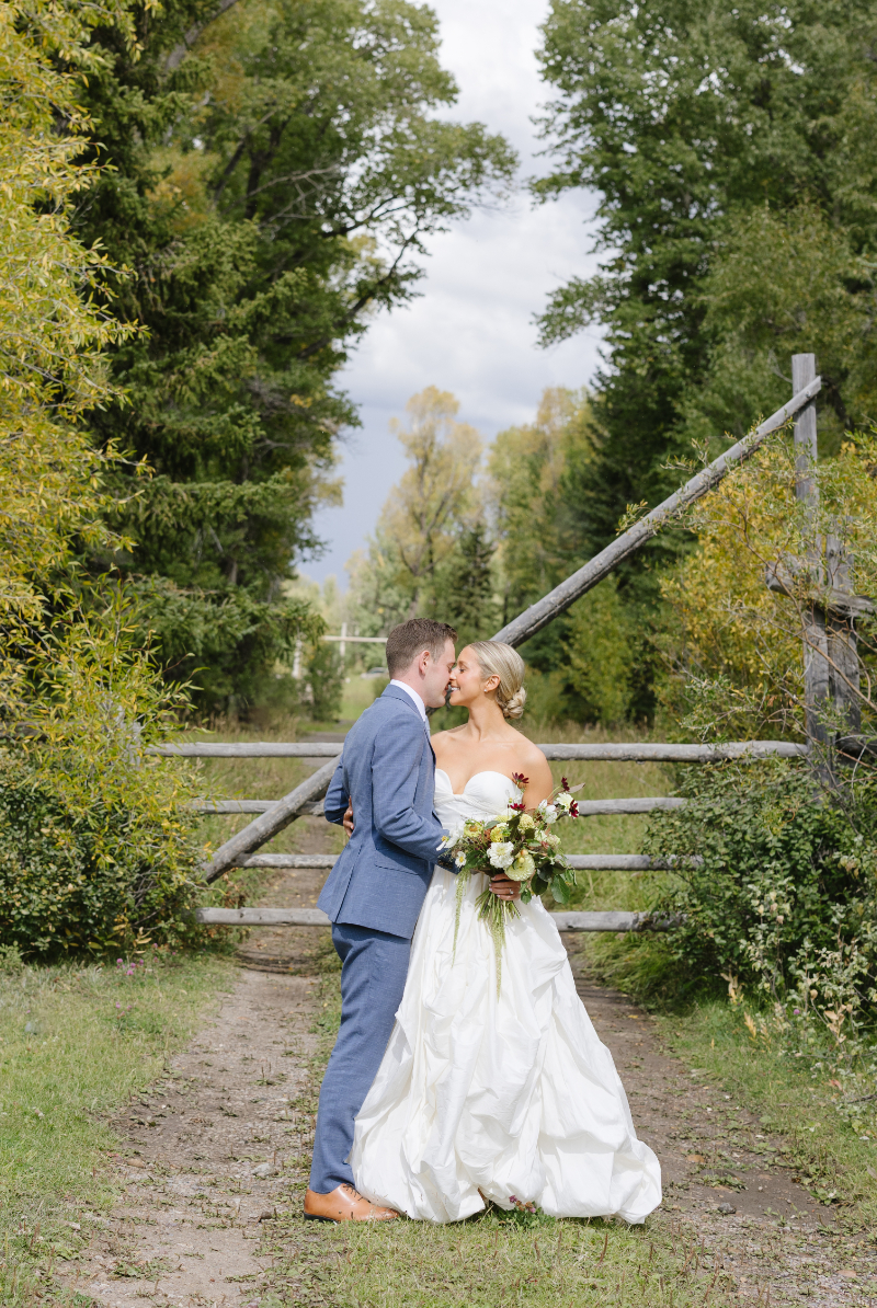 Bride and groom sharing a kiss at a rustic gate on a Jackson Hole dude ranch