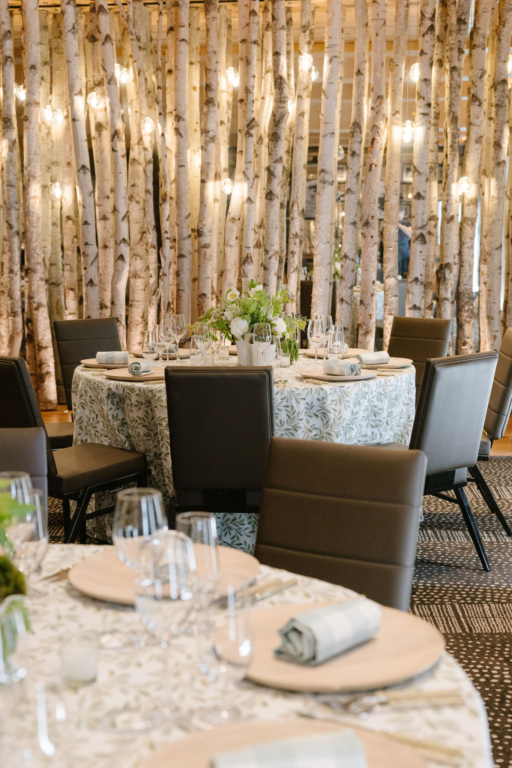 Documentary style wedding photography capturing an intimate indoor reception with birch tree installation, soft lighting, and refined table settings