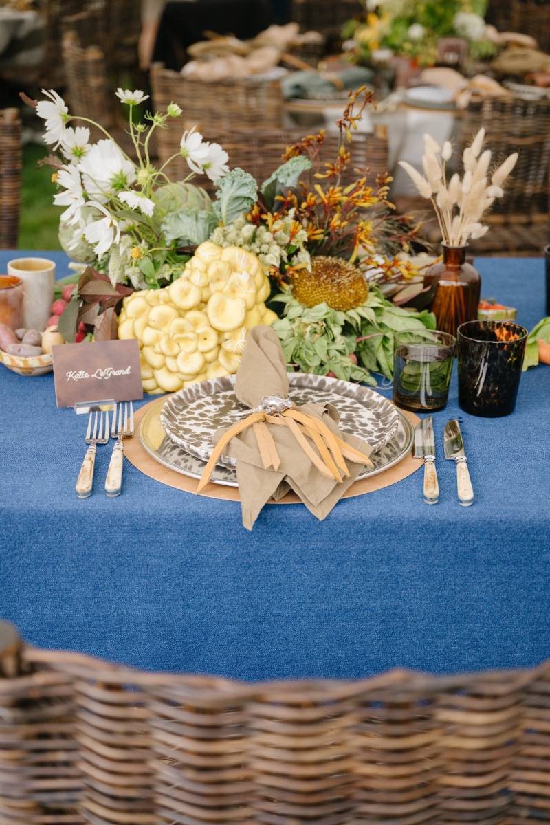 Close-up documentary style wedding photography of a detailed place setting with organic florals and layered textures at an outdoor reception