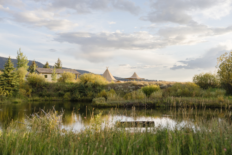 Documentary style wedding photography capturing a scenic Jackson Hole landscape with a tented reception set against mountains and reflective water at sunset