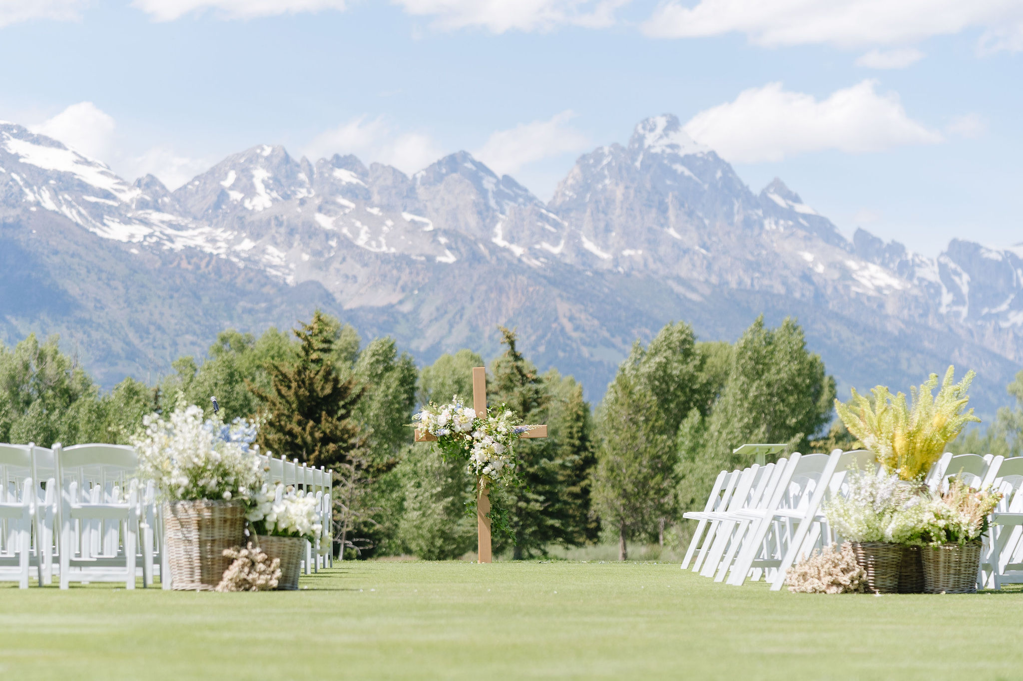 Documentary style wedding photography capturing a mountain ceremony setup with floral cross and Grand Teton views in Jackson Hole