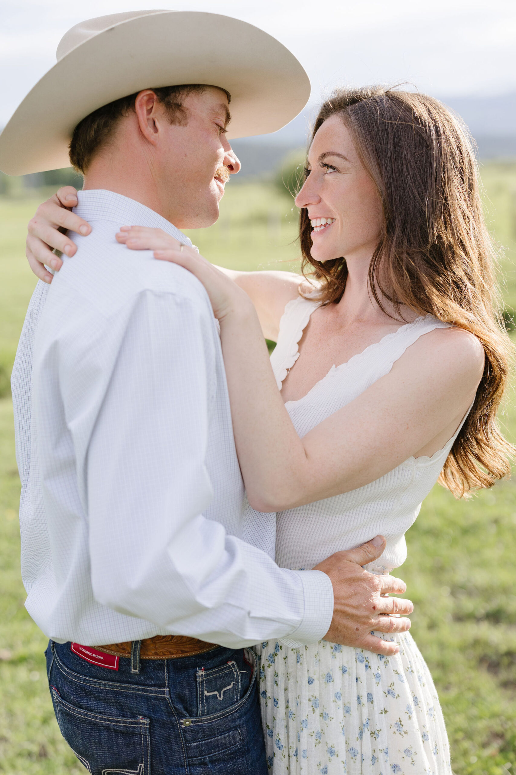 Couple embracing and smiling at each other during sunlit lake engagement photos in a natural mountain setting