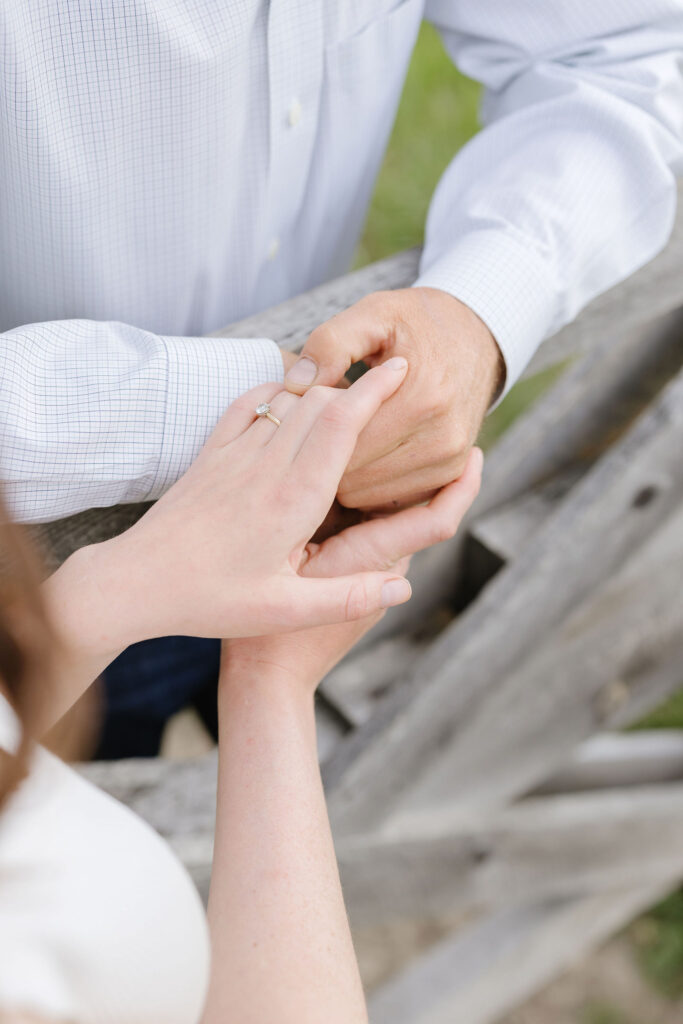 Close-up of hands showing an engagement ring as a couple holds hands by a wooden fence