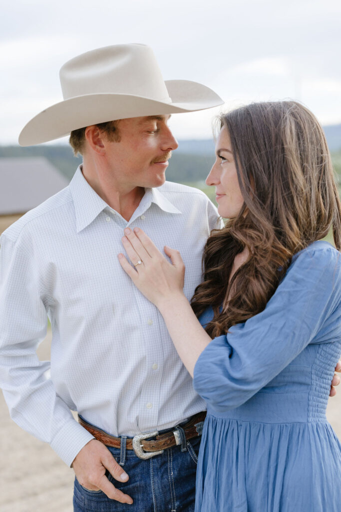 Couple smiling at each other during lake engagement photos with western-inspired outfits and soft natural light
