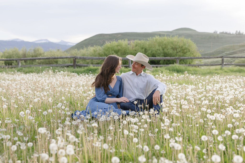 Couple sitting together in a field of wildflowers during golden hour lake engagement photos in the mountains