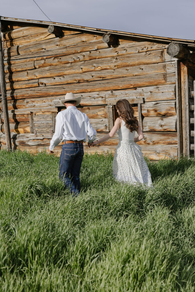 Couple walking hand in hand past a rustic cabin during natural and candid lake engagement photos